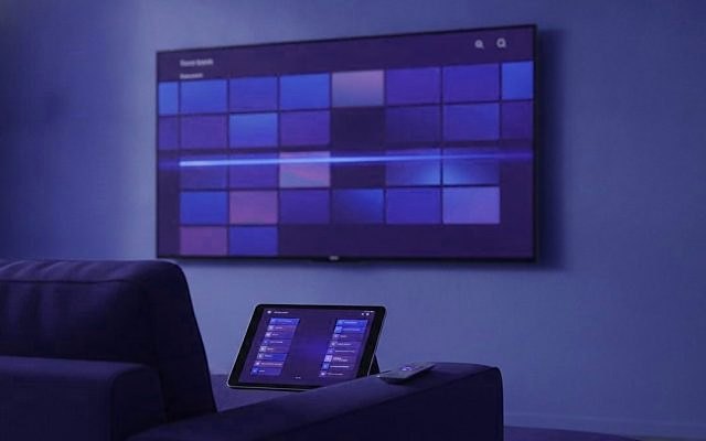 Cover for “Best IPTV apps for a long channel list: favorites, guides and catch-up”: a wall television showing a grid of channel tiles, with a tablet resting on the arm of a sofa
