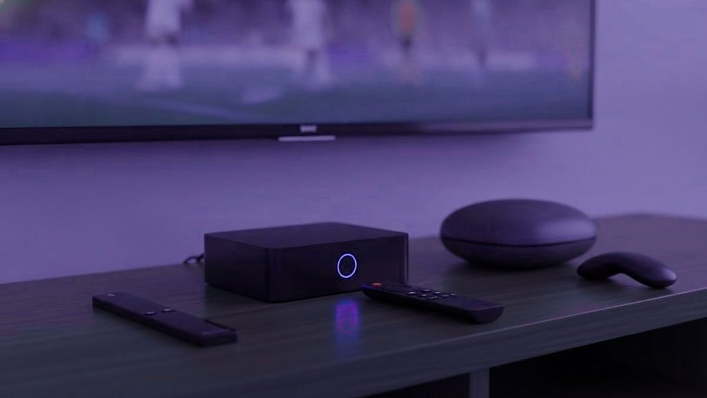 Cover for “Best IPTV box or stick: choosing what to plug in behind the TV”: a set-top box, a round streaming box and two remotes on a TV console, with a match on the screen above