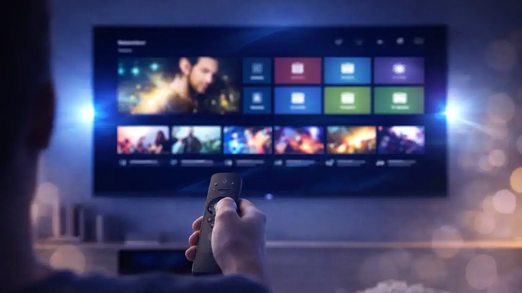 Cover for “IPTV glossary: common terms, sorted by the question behind them”: a hand pointing a remote at a large television showing a grid of films and channels in a dim room
