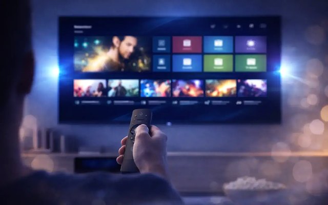 Cover for “IPTV glossary: common terms, sorted by the question behind them”: a hand pointing a remote at a large television showing a grid of films and channels in a dim room