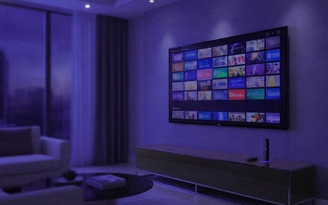 Cover for “What is IPTV? How television moved from the antenna to the internet”: a living room at dusk with a wall television showing rows of channel tiles above a low console